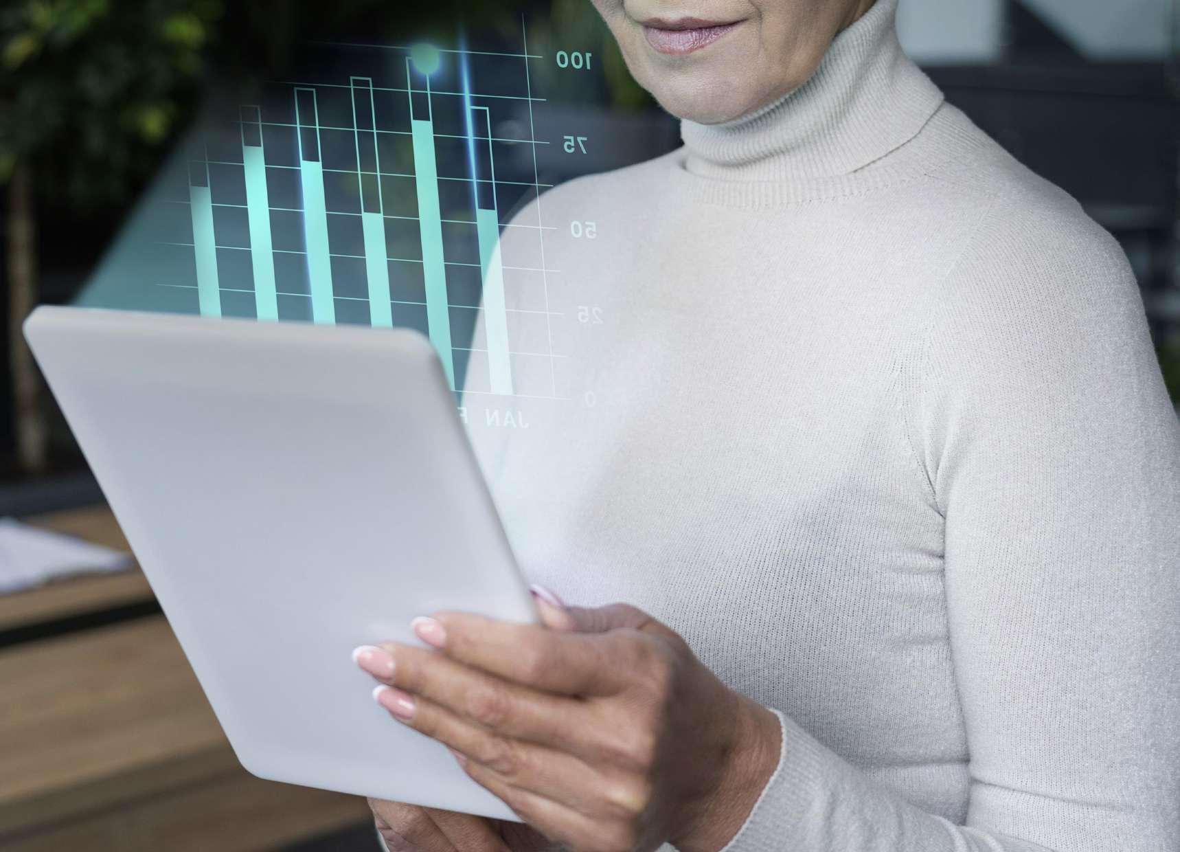 Imagem de mulher segurando tablet e projeção de gráficos para simbolizar a tecnologia e a contabilidade. 